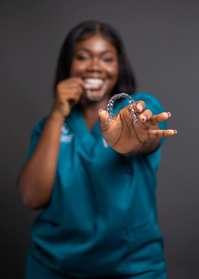 Smiling female dental professional in teal scrubs holding a clear aligner, showcasing orthodontic treatment for straighter teeth at German Ozone Medical Centre
